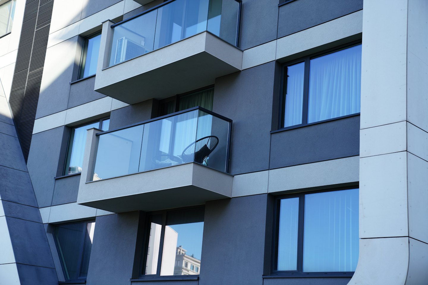 Moderne Gebäudefassade mit grauen geometrischen Paneelen und Balkonen.